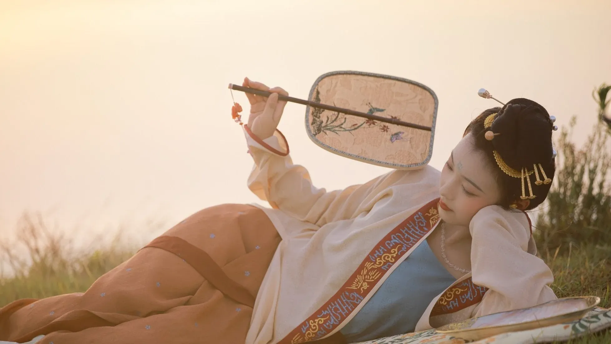 Elegant lady in authentic Song-style Hanfu reclining on grass at sunset, showcasing traditional Chinese clothing and Eastern aesthetic charm.