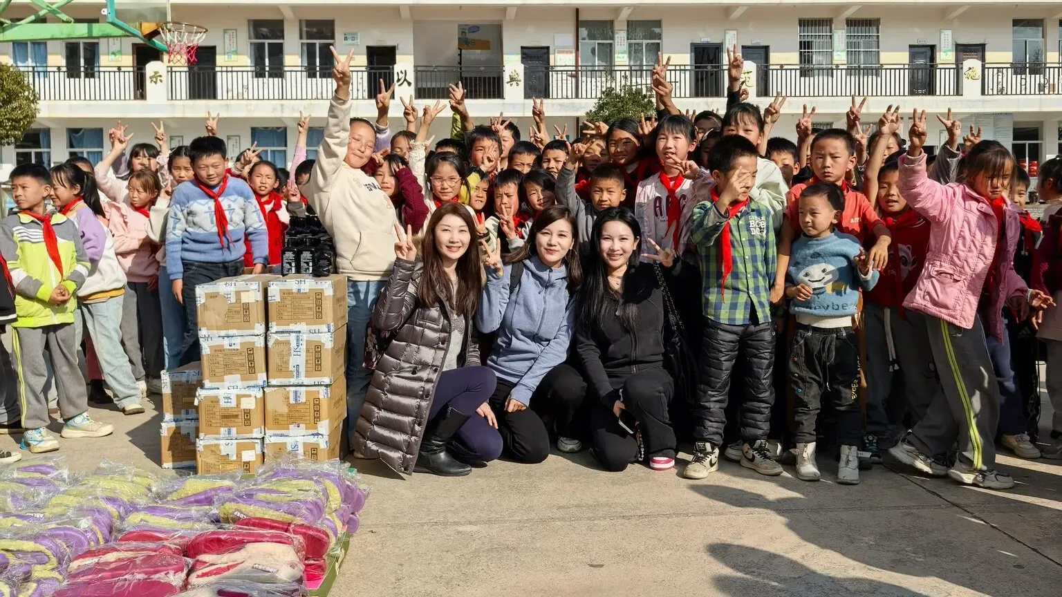 Charity donation scene in rural China - Volunteers with school children receiving supplies to support cultural education initiatives for rural kids.